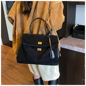 Detail of matte black suede tote bag with dual gold twist-lock closures and long strap