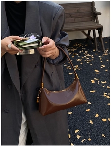 Gros plan d'un sac demi-lune en cuir verni marron avec détails dorés sur fond d'automne
