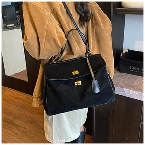 Close-up of black suede handbag with gold twist lock and shoulder strap on a model