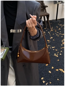 Détail du sac croissant marron brillant avec chaîne dorée tenu par un mannequin en costume