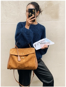 Detail of a large brown suede handbag featuring a gold twist lock and leather side panels