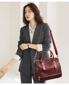 Detail of burgundy woven texture handbag with metal zippers and adjustable strap