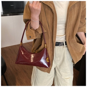 Détail du sac croissant en cuir verni rouge foncé avec boucles dorées et pendentif