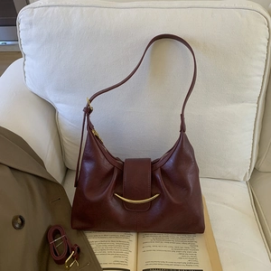 Sac à bandoulière plissé bordeaux avec garniture dorée et sangle réglable sur un livre