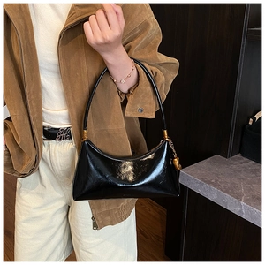 Détail d'un sac demi-lune en cuir verni noir brillant avec des ferrures dorées