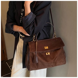 Close-up of dark brown suede handbag with golden twist-lock buckles and premium leather trim