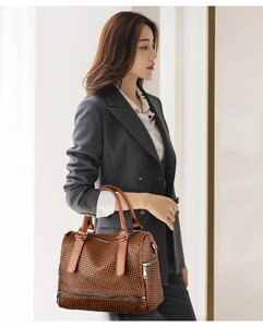 Detail of a brown woven texture Boston handbag held by a model in a professional grey suit