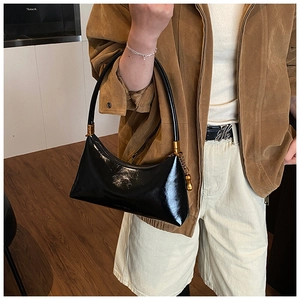 Détail d'un sac demi-lune en cuir verni noir avec ferrures dorées porté à l'épaule