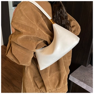 Détail du sac demi-lune blanc brillant avec finitions dorées sur manteau en daim marron