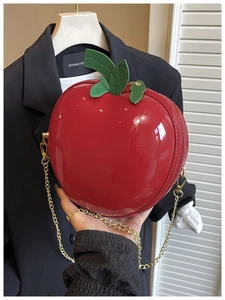 Detail view of a glossy red apple-shaped bag with green leaf and golden chain
