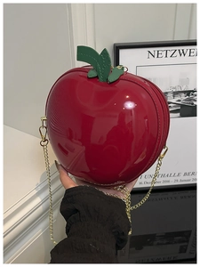 Detail of red apple-shaped crossbody bag featuring glossy patent leather and gold chain strap