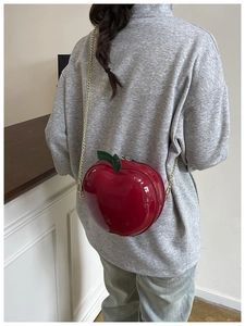 Detailed view of red apple-shaped crossbody bag with gold chain strap and green leaf detail