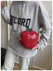 Detail of red apple-shaped crossbody bag featuring glossy finish and gold metal chain strap