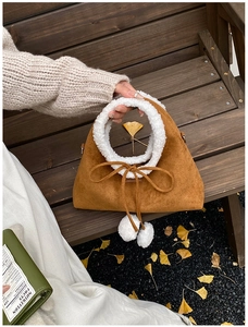 Detailed view of brown suede handbag with white faux fur trim on a wooden bench