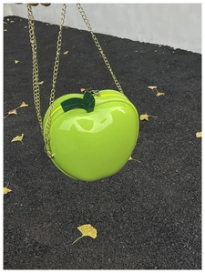 Close-up of bright green apple-shaped lacquer bag with golden chain and leaf details