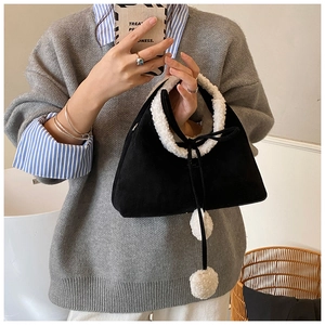 Detail of black suede handbag with white faux fur trim and cute pom-poms on long ties