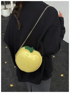 Detailed view of yellow apple-shaped shoulder bag with metallic chain and green leaf