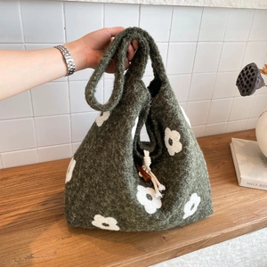 Deep green knit tote bag with white floral pattern and drawstring closure shown in hand