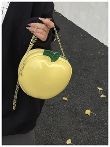 Detail of bright yellow apple-shaped crossbody bag with green leaf and golden chain
