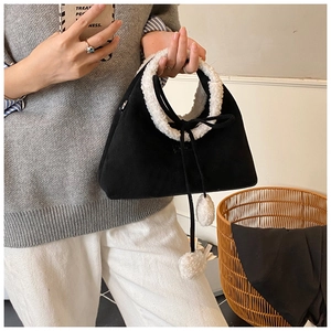 Detail of black suede handbag with white faux fur trim and cute plush ball drawstrings