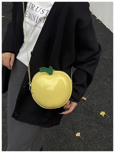 Detail of yellow apple-shaped glossy crossbody bag with green leaf and gold chain strap