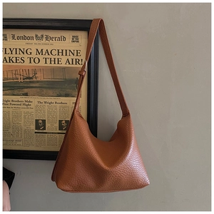 Détail d'un sac à bandoulière en cuir beige avec texture grainée et design en demi-lune