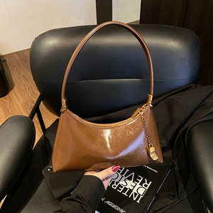 Sac croissant en cuir verni marron foncé avec breloque dorée et style minimaliste chic