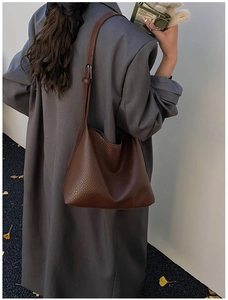 Sac hobo marron grainé porté à l'épaule par un mannequin vêtu d'un manteau gris élégant