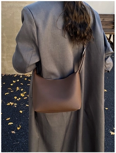 Brown lychee leather hobo bag worn by a model in a gray coat on a street with ginkgo leaves