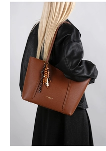 Detail of brown leather tote with tassel charm and gold logo on black leather background
