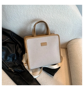 Detail of minimalist canvas handbag with brown leather trim on a cozy textured sofa