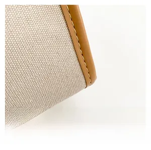 Detail of beige canvas texture with brown leather trim and contrast stitching on a handbag