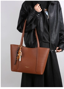 Close-up of brown pebbled leather tote bag featuring gold lettering and beaded charm