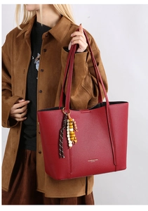 Detail of red pebbled tote bag with beaded tassel charm and gold logo on shoulder