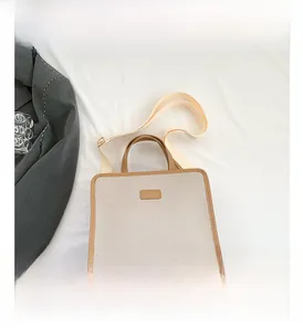 Detail of square canvas tote bag featuring brown leather trim and fabric shoulder strap
