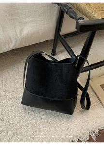 Détail d'un sac seau noir rétro contrastant suède et cuir lisse sur tapis blanc