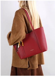 Detail of red leather tote bag with lychee texture and colorful wooden bead charm