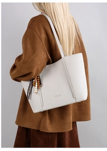 Detail of white lychee pattern leather tote bag with wooden bead tassel on a model