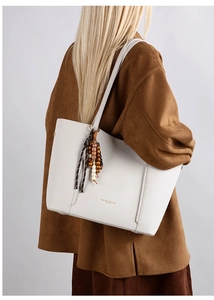 Detail of white pebbled leather tote bag with gold logo and beaded tassel charm accent