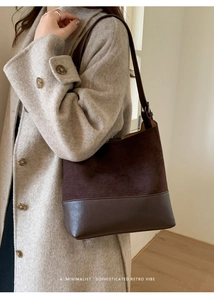 Détail du sac seau rétro en daim marron avec coutures bi-matière sur un manteau beige