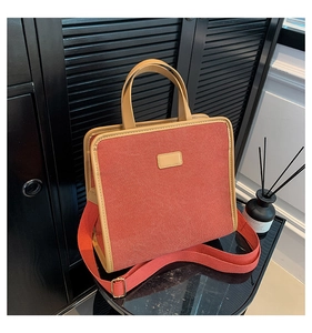 Detail view of brick red canvas tote featuring tan leather trim and adjustable strap