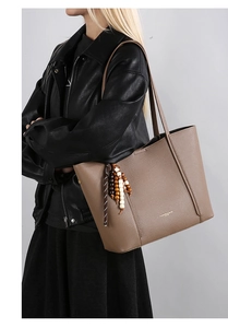 Close-up of brown pebbled leather tote bag with wooden bead tassel and gold lettering