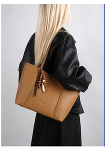 Detail of tan brown pebble leather tote bag with ethnic wooden bead charm on model