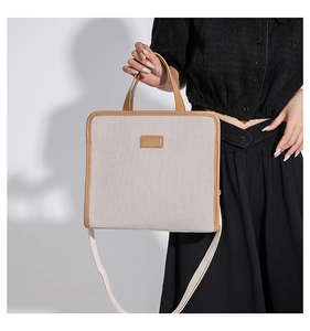 Detailed close-up of a minimalist canvas handbag with brown leather trim and shoulder strap