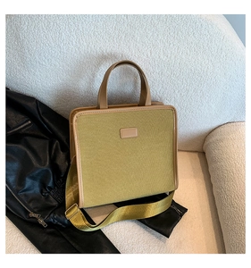 Detail of a mustard yellow canvas tote bag with brown leather trim on a white sofa