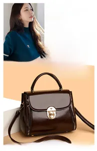 Detail of dark brown glossy leather handbag featuring golden twist lock and adjustable strap