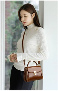 Detailed view of brown leather handbag with gold metal twist lock and shoulder strap