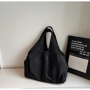 Detail of minimalist black nylon tote bag with wide straps on white marble