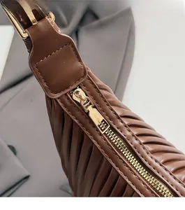 Détail du zip doré fluide et de la texture en cuir marron plissé sur un sac à main