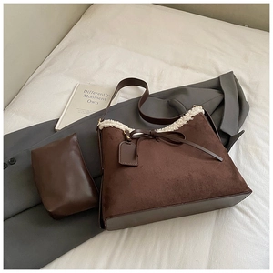 Detailansicht der braunen Wildledertasche mit Fleecebesatz und Lederschleife auf Bett